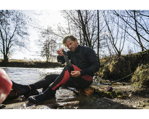 Muž si u vody obléká neoprenové ponožky