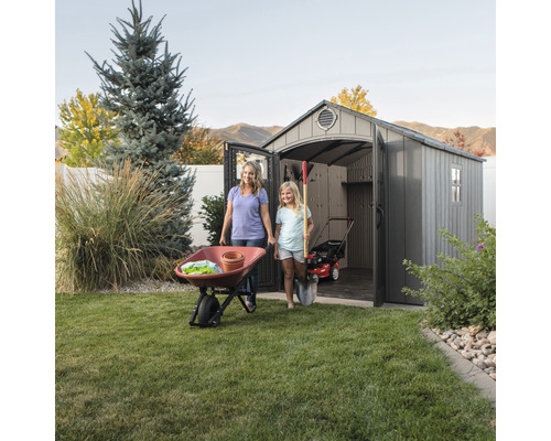 Scéna s matkou, dítětem, zahradní kůlnou, kolečkem a zahradním nářadím na zahradě.