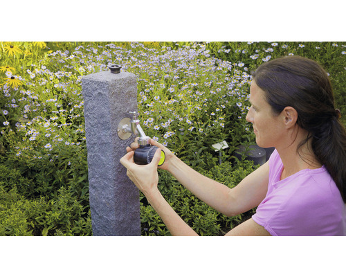 Žena připojuje zavlažovací počítač k vodovodnímu kohoutku na zahradě.