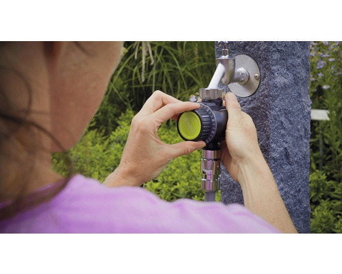 Žena ovládá zavlažovací počítač na vodovodním kohoutku na zahradě.