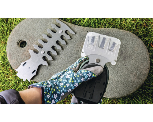 Ruka se zahradní rukavicí drží ostřič nůžek na živý plot, vedle zařízení pro zarovnávání nůžek na živý plot