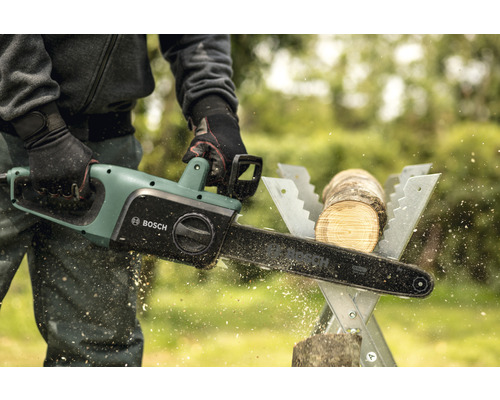 Osoba řeže kus dřeva na koze elektrickou řetězovou pilou Bosch.