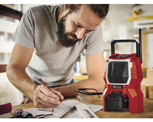 Muž si dělá poznámky vedle červeného staveništního rádia značky Einhell.