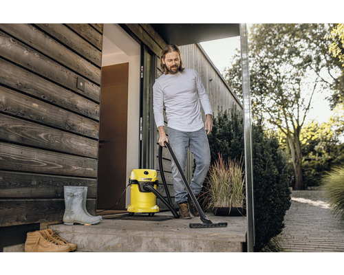 Muž čistí terasu před domem mokro suchým vysavačem. V pozadí jsou vidět rostliny.