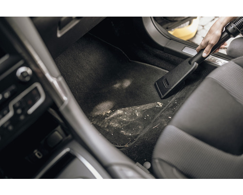 Osoba vysává špinavý prostor pro nohy v autě pomocí vysavače.