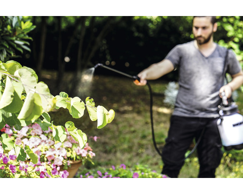 Muž používá zahradní postřikovač pro ošetřování rostlin