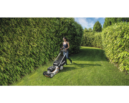 Žena seče trávník sekačkou na zahradě s bambusovými živými ploty.