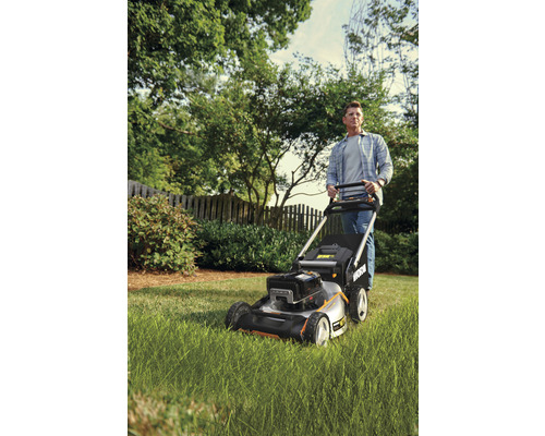 Muž tlačí sekačku na trávu na zahradě.