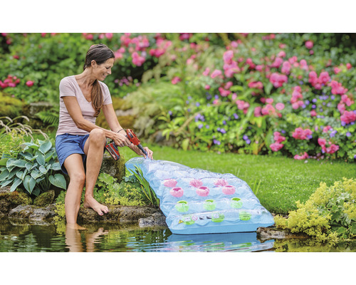 Žena instaluje plovoucí jezírkový filtr s akumulátorovým šroubovákem na zahradní jezírko.