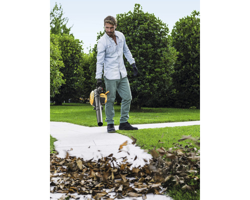 Muž používá žlutý vysavač listí na zahradě k odstranění listí.