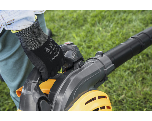 Osoba obsluhuje vysavač listí na zahradě a má na sobě rukavice.