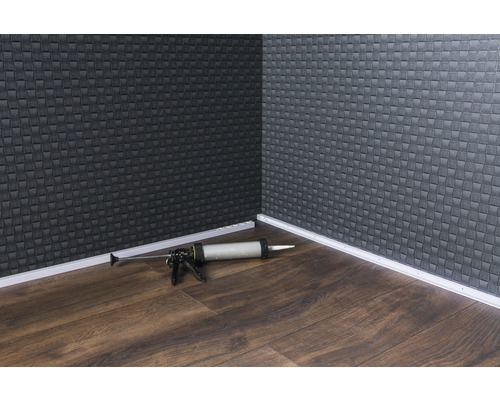 Rohová oblast místnosti s podlahovými lištami a pistolí na kartuše na dřevěné podlaze