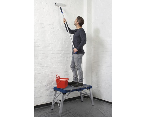 Muž maluje stěnu válečkem z pracovní plošiny.
