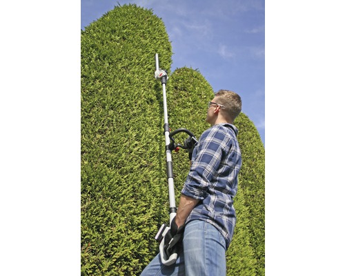 Muž stříhá vysoký živý plot pomocí plotostřihu s teleskopickou tyčí