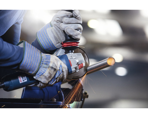 Osoba brousí kovovou trubku úhlovou bruskou ve svěráku