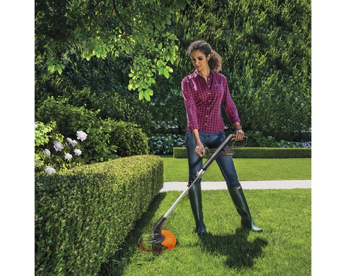 Žena stříhá živý plot s vyžínačem trávy na zahradě.