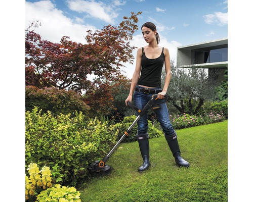 Žena pracuje se sekačkou na trávu na zahradě.