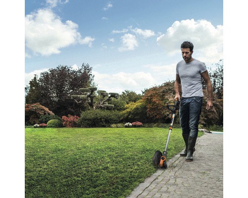 Muž používá v zahradě nůžky na trávu k zastřihování okrajů trávníku.