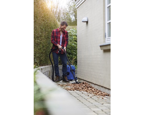 Muž uklízí mokrým a suchým vysavačem listí z dlážděné cesty.