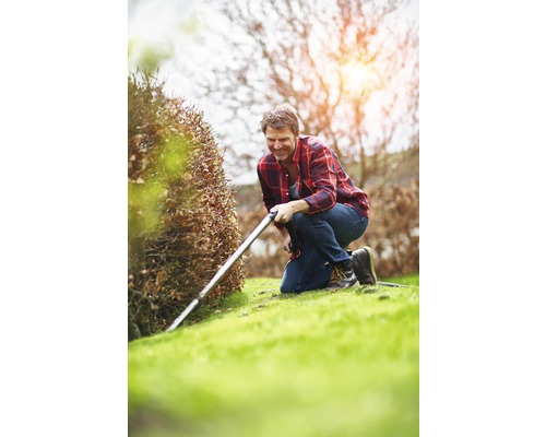 Muž klečí na zahradě a stříhá živý plot nůžkami na živý plot.