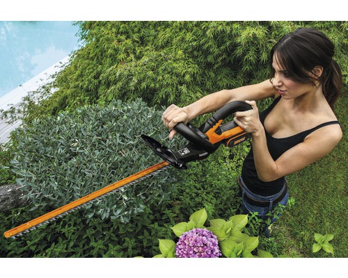 Žena stříhá živý plot akumulátorovými nůžkami na živý plot na zahradě