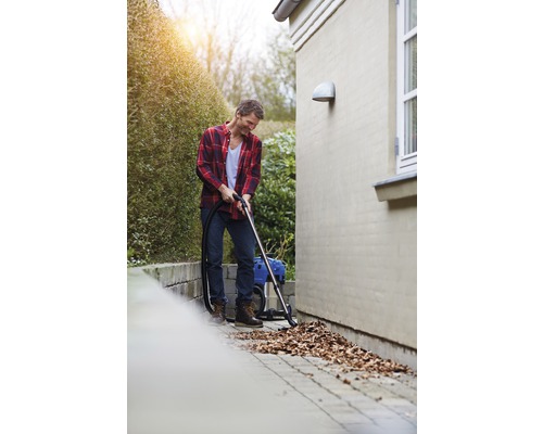 Muž vysává listí mokro suchým vysavačem na zahradě.