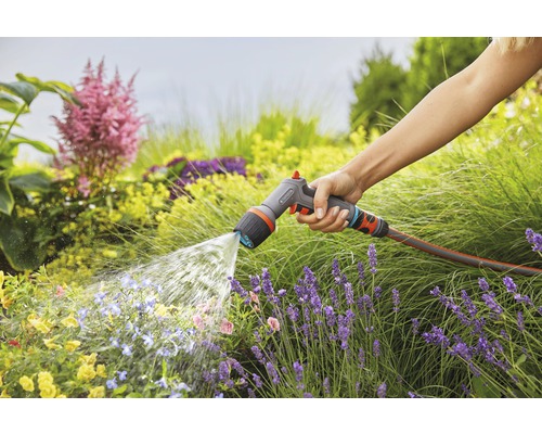 Osoba zalévá zahradu zahradní stříkací pistolí Gardena.