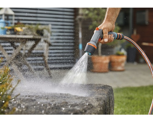 Osoba zavlažuje kámen zahradní sprchou a zahradní hadicí.