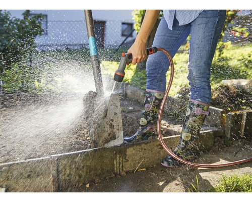 Osoba čistí zahradní lopatu zahradní hadicí.