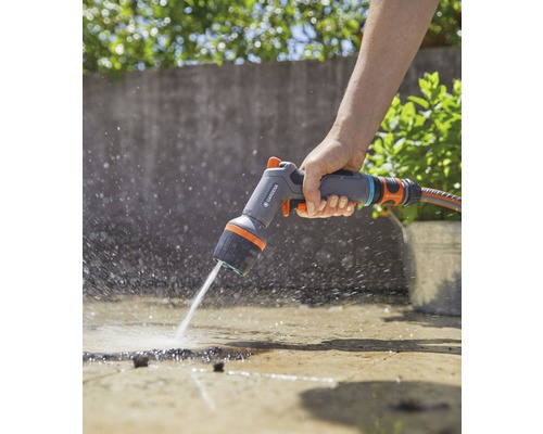 Osoba používá víceúčelovou sprchu Gardena k zavlažování povrchu.