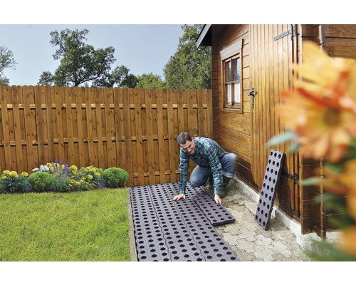 Muž pokládá zatravňovací dlaždice na zahradě poblíž dřevěné kůlny a dřevěného plotu