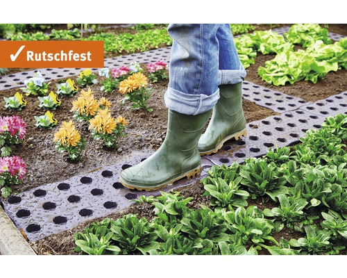 Osoba v gumových holínkách kráčí po zahradní cestě mezi rostlinami a květinami. Protiskluzové.