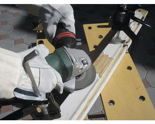 Osoba v rukavicích brousí obrobek úhlovou bruskou, upevněný pomocí pracovního stolu.