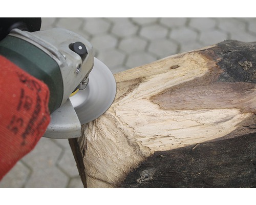 Osoba opracovává kus dřeva pomocí úhlové brusky.