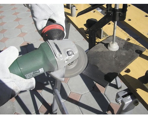 Osoba brousí obrobek úhlovou bruskou na pracovním stole.