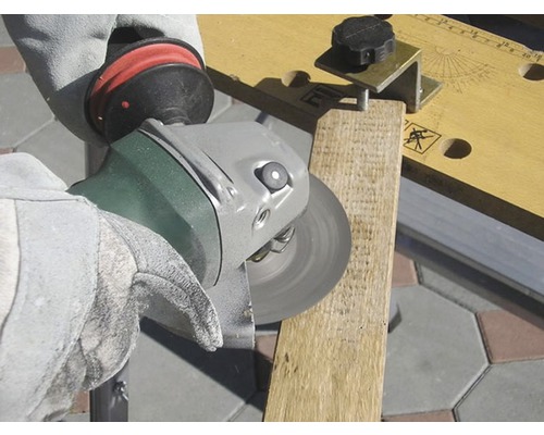 Osoba brousí dřevěnou desku úhlovou bruskou. Osoba má rukavice.
