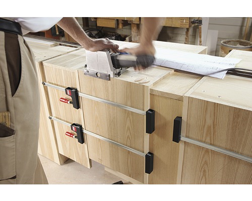 Řemeslník pracuje s lamelovací frézkou na dřevěném nábytku upevněném svorkami.