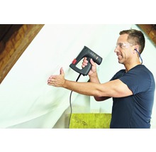 Řemeslník připevňuje fólii elektrickou sešívačkou v podkroví.