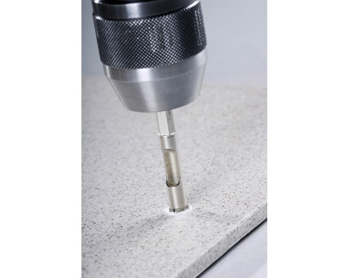 Detailní pohled na vrtačku s vrtákem do dlaždic, která vrtá otvor do dlaždice.