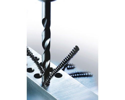 Vrták vrtá otvor do kusu kovu vedle několika šroubů.