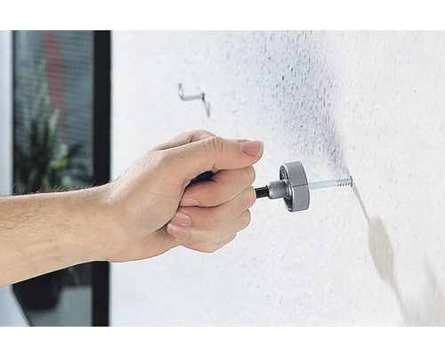 Osoba připevňuje hmoždinku ke zdi montážním nástrojem