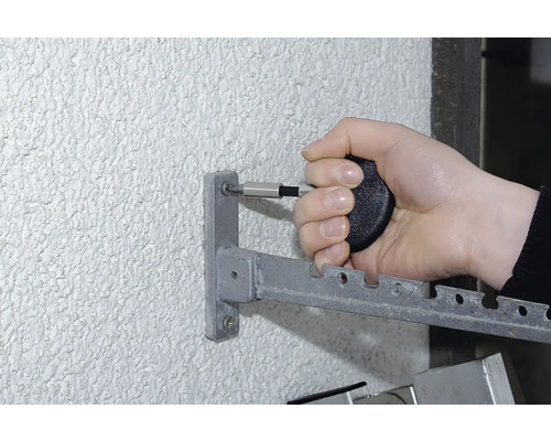 Osoba připevňuje kovový sušák na prádlo ke stěně pomocí šroubováku.