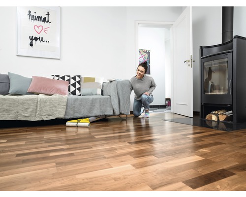 Žena používá žlutý mopovací robot v obývacím pokoji s pohovkou, krbem a dřevěnou podlahou.