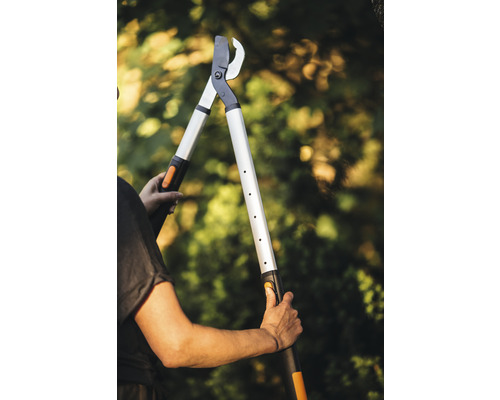 Osoba drží nůžky na větve s dlouhou rukojetí