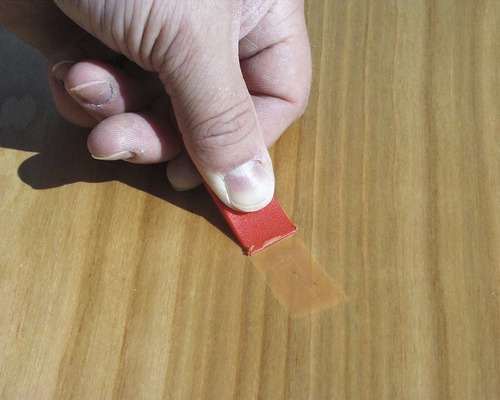 Ruka odstraňuje lepicí pásku ze dřeva