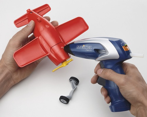 Osoba používá tavnou pistoli k opravě červeného modelu letadla