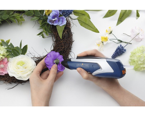 Žena připevňuje dekorace tavnou pistolí na věnec