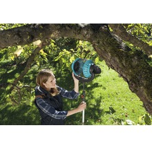 Žena používá sběrač ovoce v zahradě pod stromem.