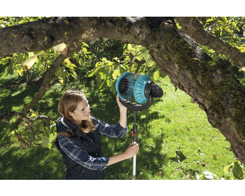 Žena používá sběrač ovoce v zahradě pod stromem.