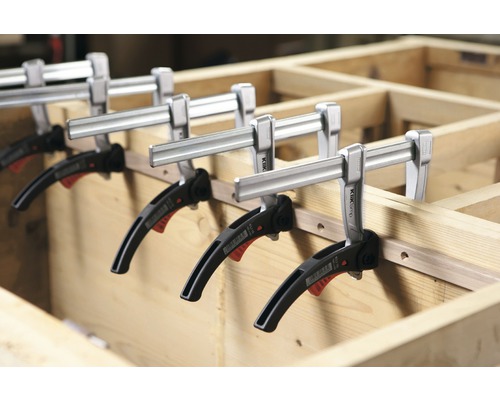 Několik svorek pro jednu ruku fixuje dřevěný obrobek.